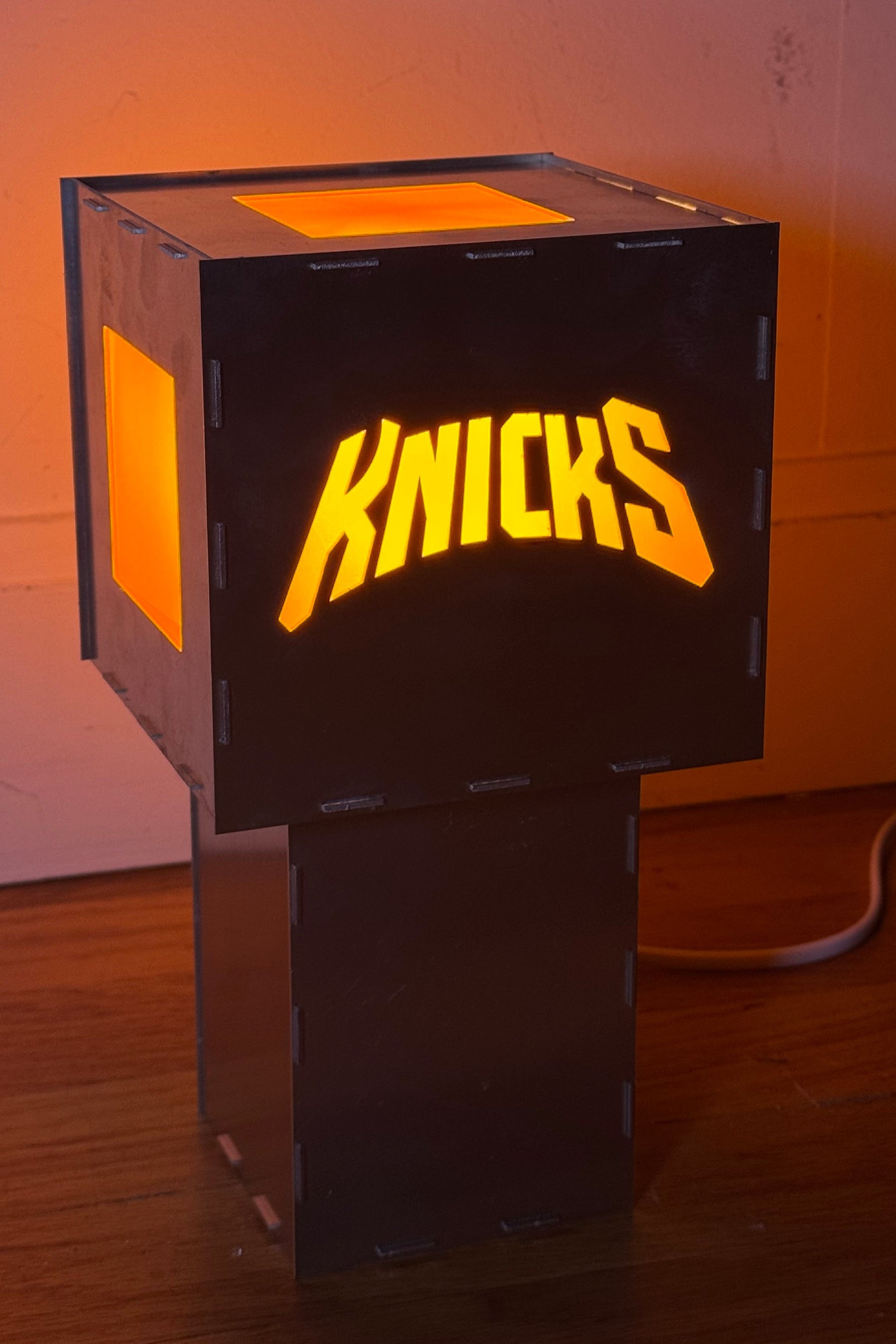Aluminum lamp with 'Knicks' logo in orange on a wooden surface