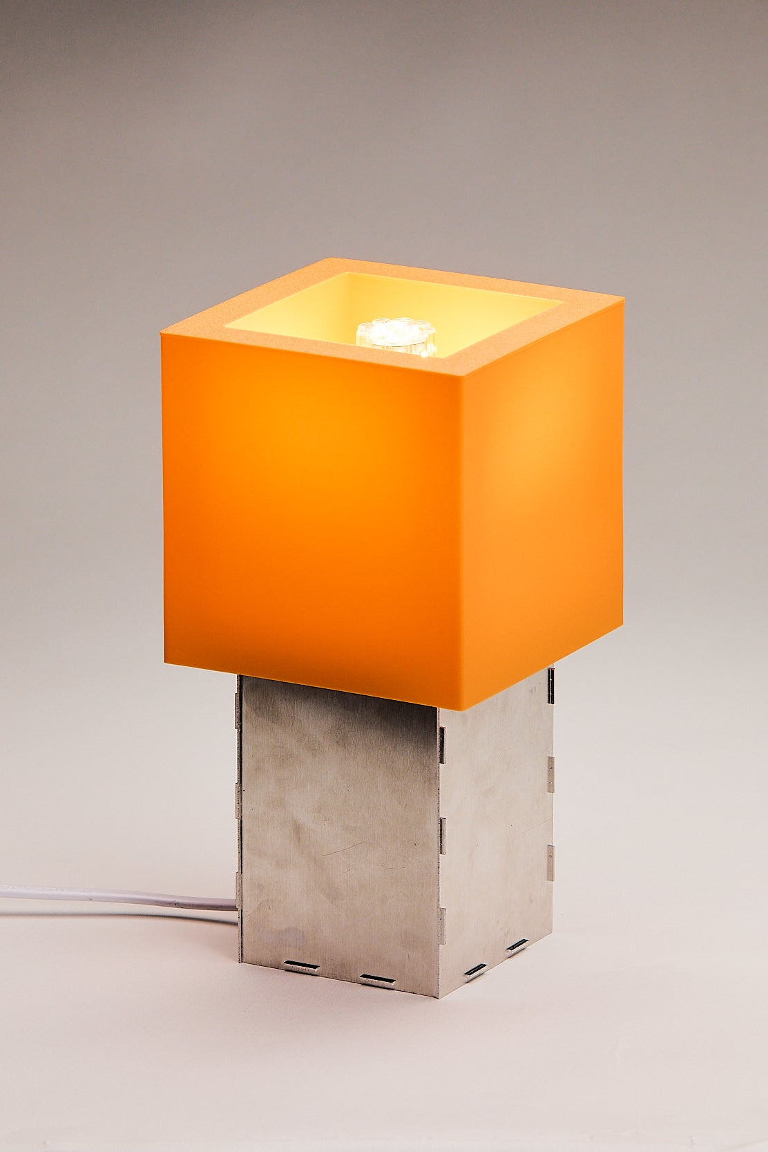 Table lamp with orange square shade and metallic base on a neutral background